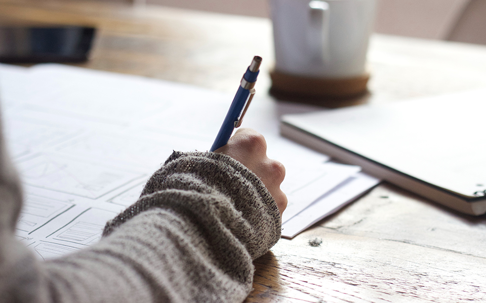 Individual writing on a paper with a pen at a desk.